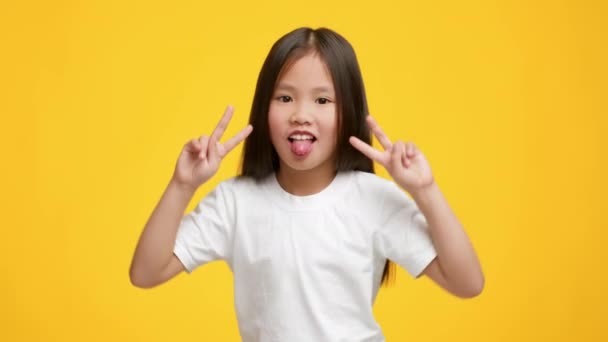 Азіатська маленька дівчинка жестикулює Перемога Скріплення язика, жовтий фон
 - Кадри, відео