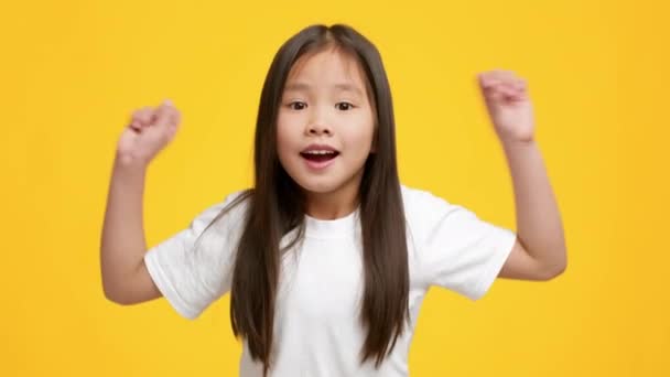 Happy školka japonská dívka třesoucí se pěsti slaví úspěch, žluté pozadí - Záběry, video