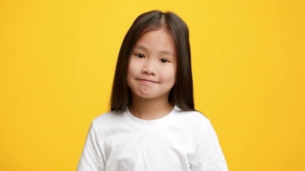 clueless aziatisch klein meisje shrugging schouders poseren over gele achtergrond - Video