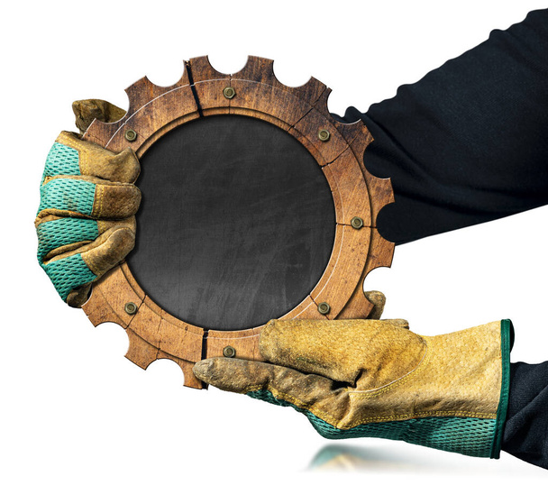 Trabajador manual con guantes de trabajo sosteniendo una rueda dentada de madera con pizarra vacía en el interior. Aislado sobre fondo blanco con espacio de copia. - Foto, imagen