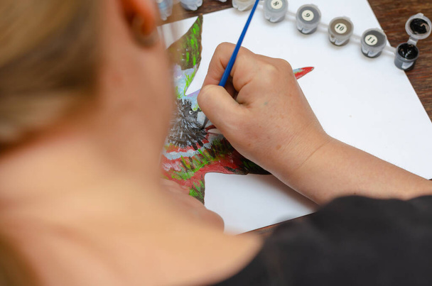 Een volwassen vrouw schildert een tekening op een droog esdoornblad. Teken een beetje egel met acryl en gouache verf. Creativiteit, schilderen. Binnen. Selectieve focus. - Foto, afbeelding