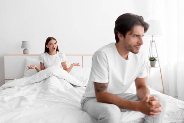 Unhappy frustration european young man ignoring angry woman, lady sits in bed and scream on guy in white bedroom - Photo, Image