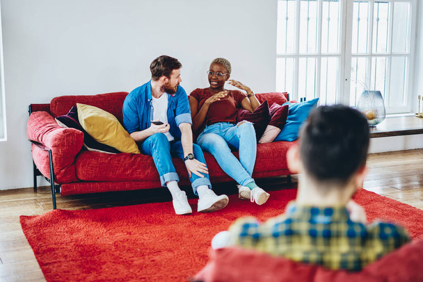 Group of young men and woman dressed in casual wear communicating with each other during resting pastime at home apartment, multicultural best friends enjoying fellow meeting in comfortable flat - Foto, Bild