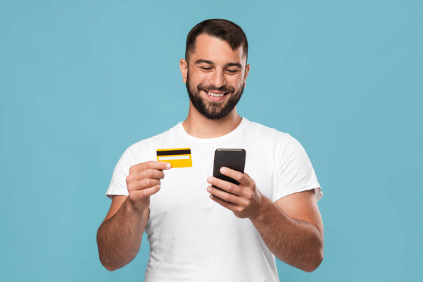 Neşeli orta yaşlı yakışıklı Avrupalı erkek mal sipariş ediyor, kredi kartı ve akıllı telefon gösteriyor. - Fotoğraf, Görsel