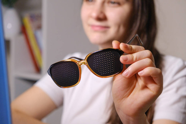 Eine Frau hält eine Perforationsbrille, um Sehstörungen zu korrigieren. - Foto, Bild