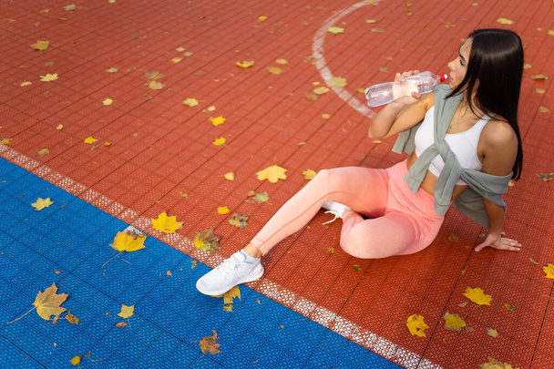 Athletic girl with a bottle of water in hands sits on a basketball court	 - Photo, Image
