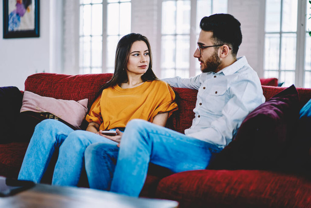 Multicultural couple in love talking and discussing plans during weeknd time in apartment, Turkish boyfriend communicating with Caucasian girlfriend resting at cozy sofa in stylish living room - Foto, Bild