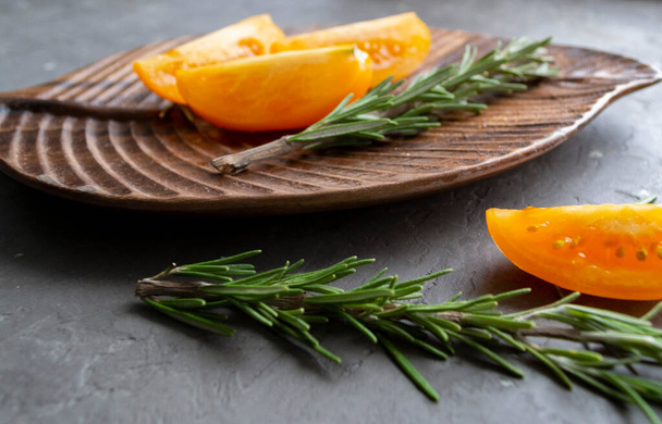 Yellow sliced tomatoes with rosemary on a wooden tray, on a concrete background - Fotografie, Obrázek