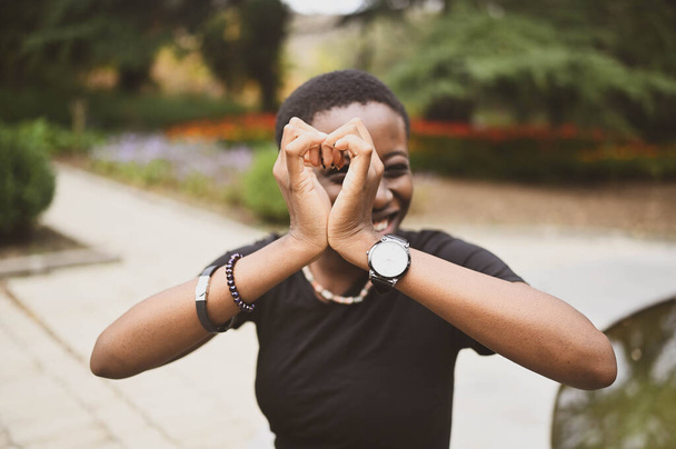 Lähikuva muotokuva houkutteleva onnellinen hymyilevä nuori luonnonkauneus lyhytkarvainen Afrikkalainen nainen yllään musta t-paita nauraa ojentaa kädet sulkemalla kameran luonto kesäpuisto. - Valokuva, kuva