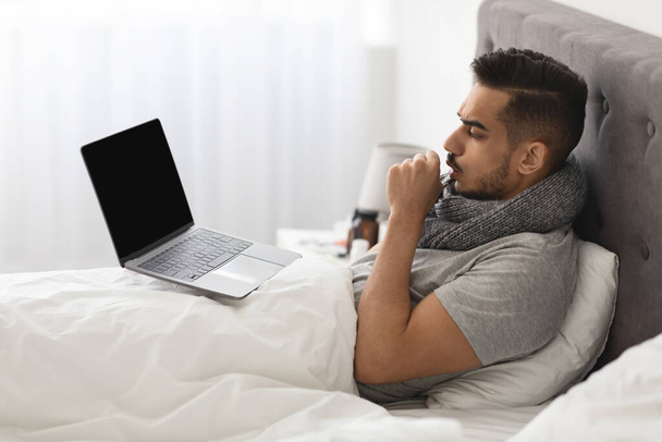 Хвора арабська людина використовує ноутбук комп'ютер сидячи в ліжку вдома
 - Фото, зображення