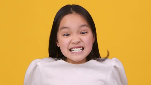 Çocukların öfkesi. Duygusal küçük Asyalı kız kameraya bağırıyor, olumsuz duyguları çığlıkla ifade ediyor, turuncu arka plan. - Video, Çekim
