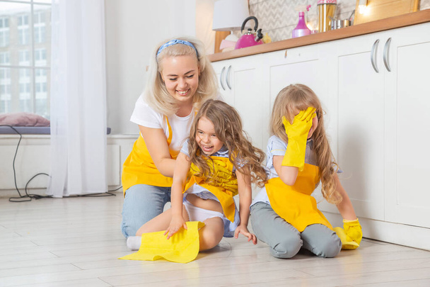 Smiling caucasian mom teaching daughters wet cleaning the kitchen. Two female generations family together in kitchen. - Fotó, kép