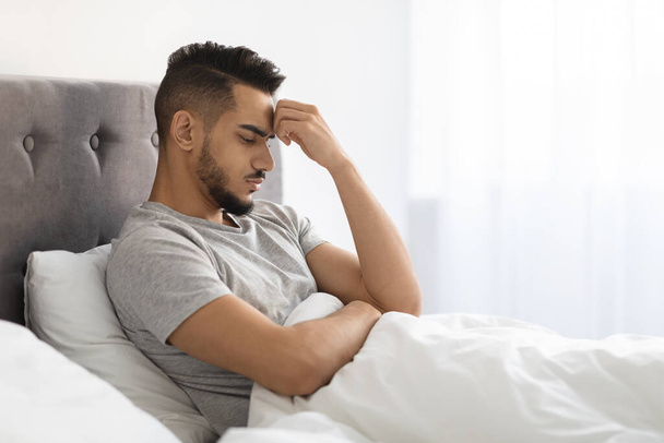 Depressionskonzept. Aufgebrachter junger arabischer Mann sitzt im Bett und denkt über Probleme nach - Foto, Bild