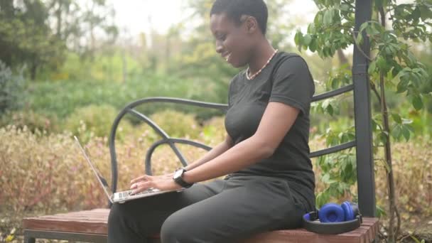 Atractivo feliz elegante africano negro de pelo corto estudiante afro pelo que estudia en línea de trabajo en el ordenador portátil en el parque verde de verano. Diversidad. Trabajo remoto, educación a distancia. - Metraje, vídeo