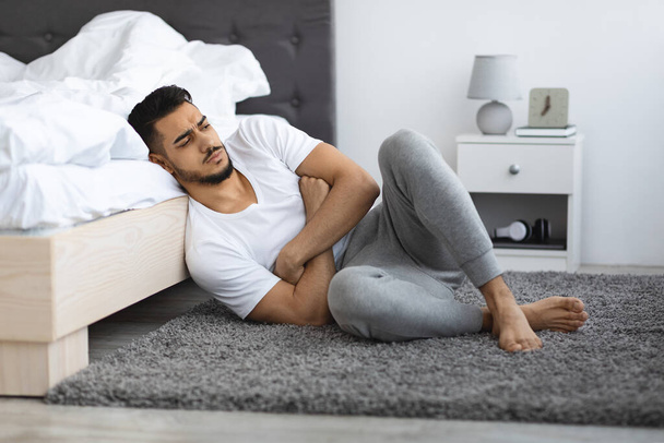 Депрессивный расстроенный молодой человек с Ближнего Востока сидит на полу в спальне - Фото, изображение