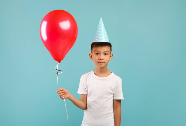 Πορτρέτο του χαριτωμένο μικρό ασιατικό αγόρι φορώντας καπέλο κόμμα κρατώντας κόκκινο μπαλόνι - Φωτογραφία, εικόνα