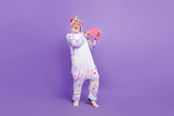Photo of dreamy funny man pensioner unicorn sleepwear holding pink heart dancing smiling isolated violet color background - Foto, Bild