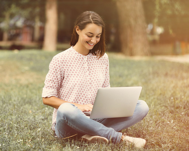 Jeune femme avec ordinateur portable assis sur l'herbe verte
 - Photo, image
