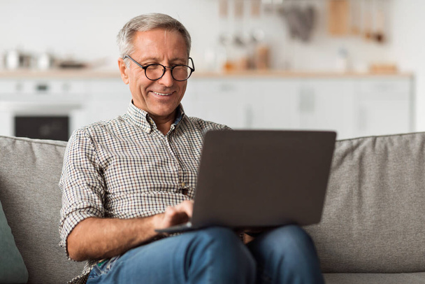 Glücklicher Senior mit Laptop surft zu Hause im Internet - Foto, Bild