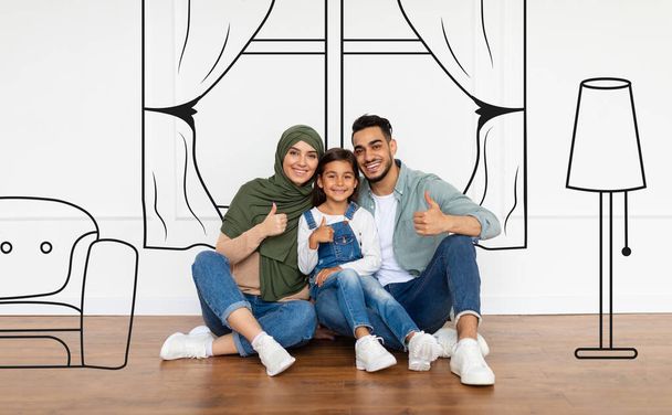Ευτυχισμένος αραβικός οικογενειακός προγραμματισμός νέο εσωτερικό σπίτι, δείχνει τους αντίχειρες επάνω - Φωτογραφία, εικόνα