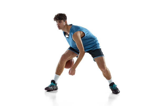 Full length portrait of basketball player practicing isolated on white studio background. Tall muscular athlete dribbling the ball. - Foto, Imagen