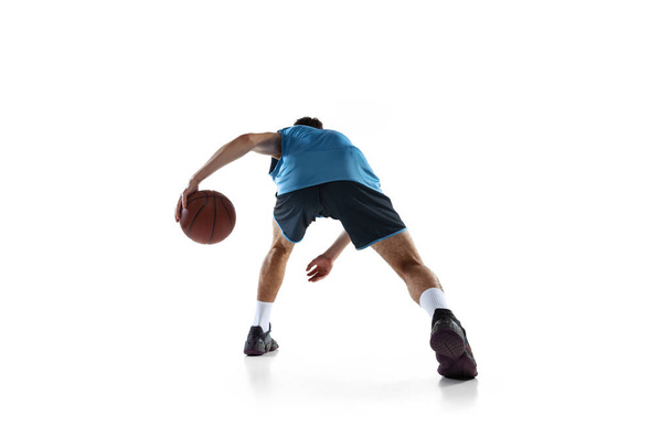 Back view of professional basketball player in blue sports uniform training isolated on white studio background. - 写真・画像