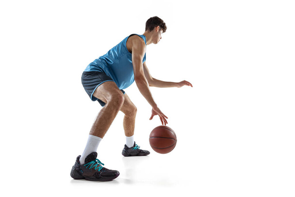 Full length portrait of basketball player practicing isolated on white studio background. Tall muscular athlete dribbling the ball. - Foto, Imagem