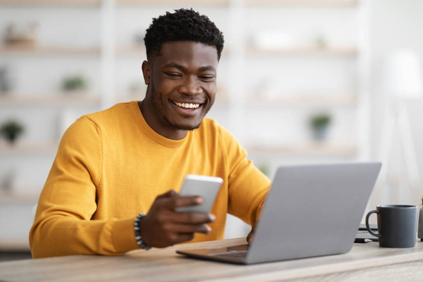 Jovem empresário negro trabalhando no laptop e usando celular - Foto, Imagem