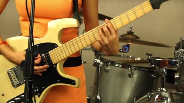 Beautiful girl plays the electric guitar. Musician in a bright orange dress. Designer stringed musical instrument of light color. Recording in a professional music studio. Perfect acoustic sounds - Footage, Video