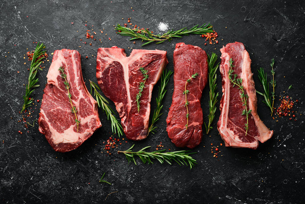 Variety of raw black Angus Prime meat steaks: t-bone, striploin, Rib eye, new york steak. Top view. On a stone background. - Фото, изображение