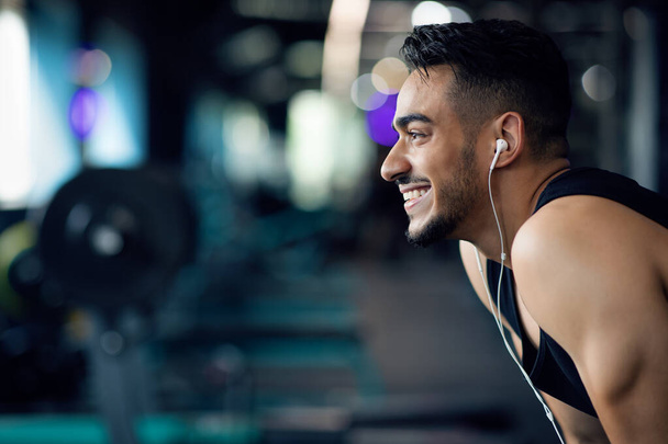 Playlist For Sport. Homem árabe sorridente ouvindo música em fones de ouvido no ginásio - Foto, Imagem