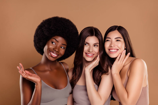Photo of dreamy fancy three best friends wear crop tops smiling hug looking empty space isolated beige color background - Photo, Image