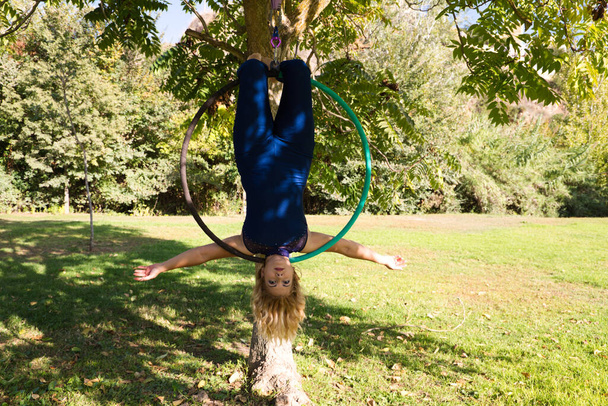 Blondi nainen ja nuori voimistelija akrobaatti urheilija suorittaa antenni liikunta ilmarengas ulkona puistossa. Lithe nainen sinisessä puvussa suorittaa aiheuttaa sirkus esiintyjät tanssia lonkat. - Valokuva, kuva