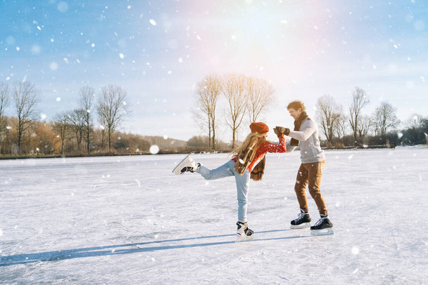 Loving couple in warm sweaters having fun on ice. Woman and man ice skating outdoors in sunny snowy day. Active date on ice arena in winter Christmas Eve. Romantic activities and lifestyle concept. - Photo, Image