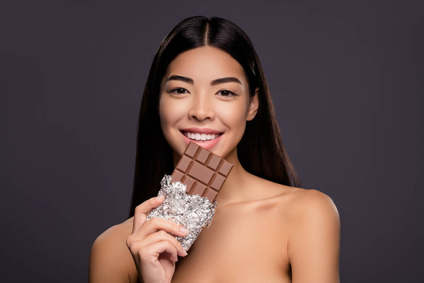 Фото веселой модели леди держать шоколад бар продвижения кондитерских продуктов изолированный серый цвет фона - Фото, изображение