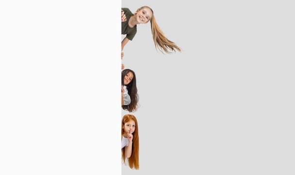 Collage of three beautiful children, kids, little girls peaking out the corner isolated over gray background - Foto, imagen