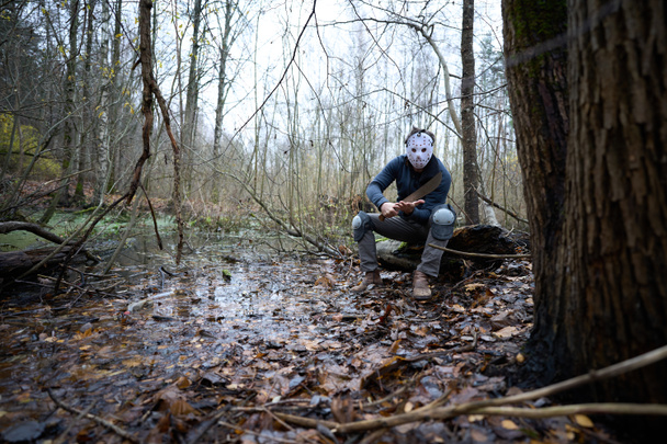 Serial killer Jason Voorhees in hockey mask and machete sitting on the swamp. Friday 13th cosplay costume.  - 写真・画像