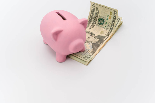pink piggy bank and dollar banknotes on a white tabletop with copy space - Foto, afbeelding