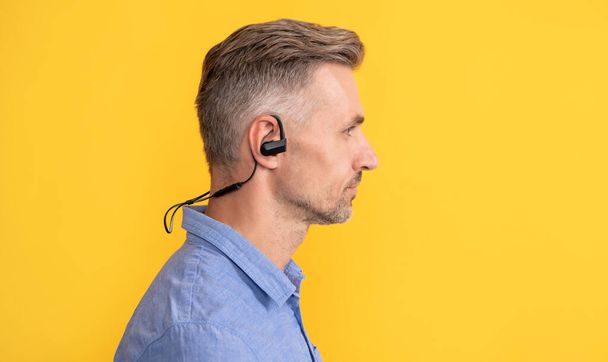 Profil des reifen Mannes mit modernen drahtlosen Kopfhörern auf gelbem Hintergrund, Technologie - Foto, Bild