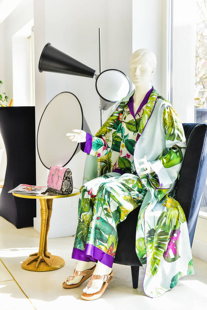 A female manikin wearing a colorful pajama and wearing a golden slipper sitting on a nice black seat - 写真・画像