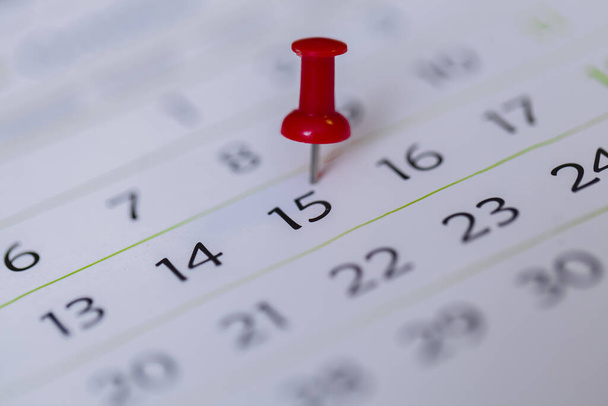 A closeup shot of a thumbtack mention the date on the calendar - Foto, Bild