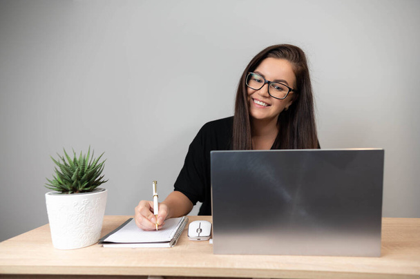 Молода ділова жінка працює в офісі з ноутбуком, роблячи нотатки
  - Фото, зображення