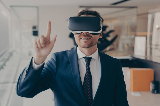 Молодий успішний бізнесмен в VR окулярах торкається повітря пальцем під час віртуальної ділової зустрічі
 - Фото, зображення