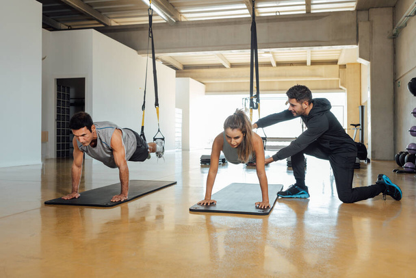 Treinador de fitness ajuda homem e mulher a fazer posição de prancha em um ginásio. - Foto, Imagem