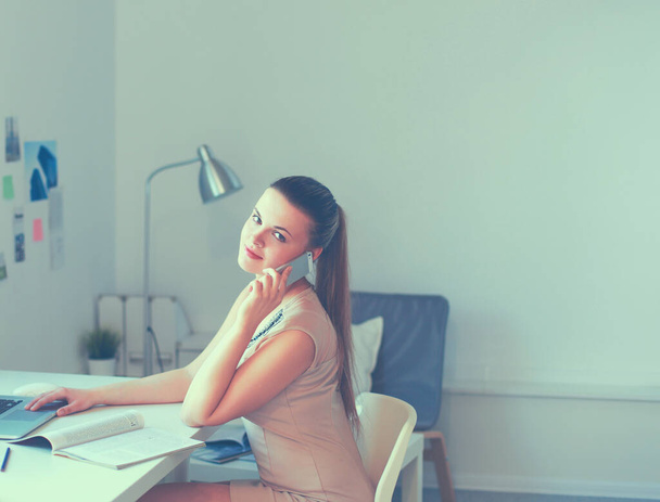 Young businesswoman sitting at the desk and talking on phone - Fotoğraf, Görsel