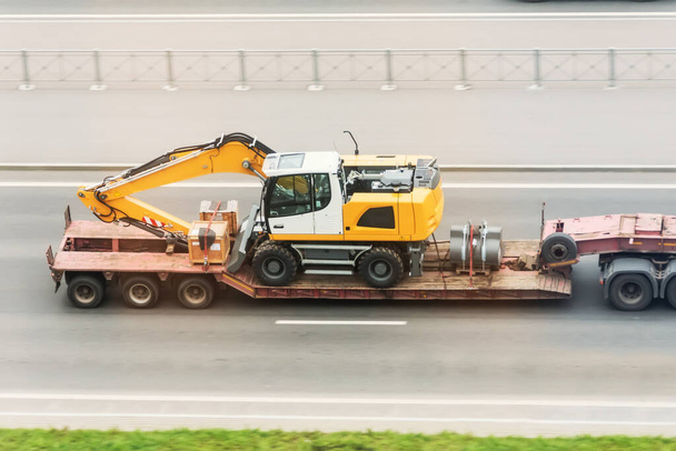 Camion remorque avec plate-forme longue transporter la pelle sur l'autoroute. Logistique du transport de marchandises lourdes et surdimensionnées par route. - Photo, image