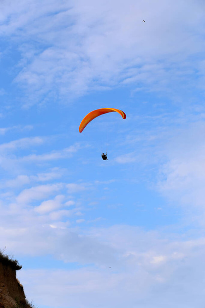 El parapente naranja vuela en el cielo azul sobre el fondo de las nubes. Parapente en el cielo en un día soleado. - Foto, imagen