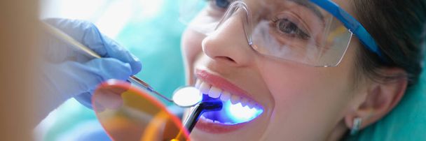 Frau mit Schutzbrille wird beim Zahnarzt mit Lichtlampe behandelt - Foto, Bild