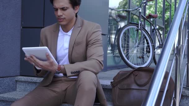 Jovem empresário sentado nas escadas e usando tablet digital
  - Filmagem, Vídeo