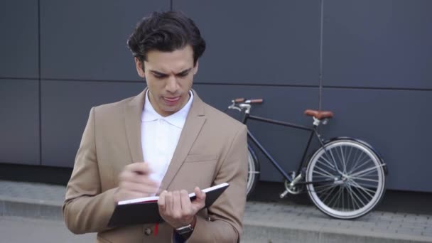 pensive businessman writing in notebook and smiling outside  - Filmagem, Vídeo
